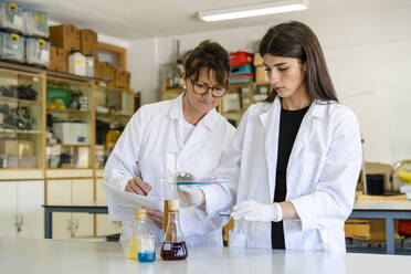 Mature female scientist with document examining chemical with colleague at laboratory - DLTSF01988