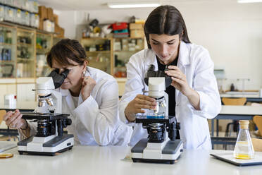 Female scientists examining chemical through microscopes at laboratory - DLTSF01992