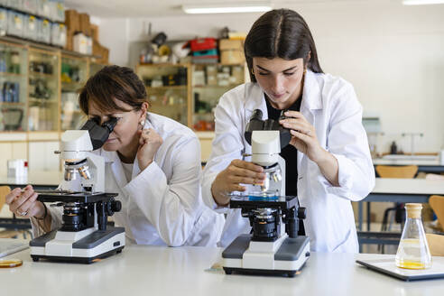 Wissenschaftlerinnen, die im Labor Chemikalien durch Mikroskope untersuchen - DLTSF01992
