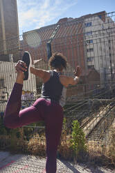 Female athlete doing stretching exercise while leaning on fence - PACF00203