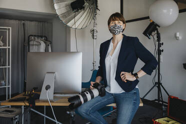 Fotografin mit Kamera auf dem Schreibtisch im Studio während einer Pandemie - MFF08251