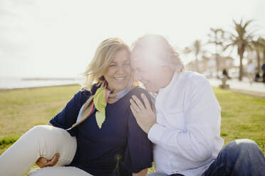 Happy mature couple sitting together on grass during vacation - GMCF00134