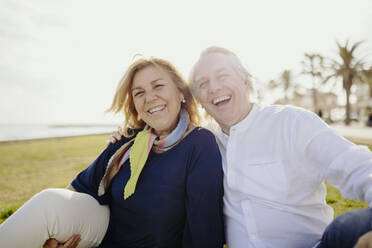 Happy mature man sitting with woman wearing scarf during vacation - GMCF00135