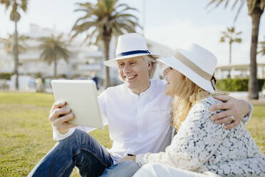 Happy mature couple wearing hats doing video call through digital tablet during vacation - GMCF00147