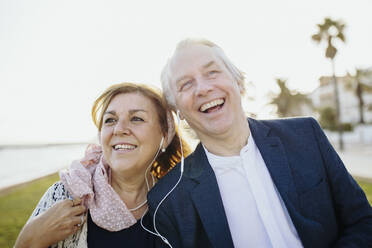 Glückliches reifes Paar hört im Urlaub Musik über In-Ear-Kopfhörer - GMCF00151
