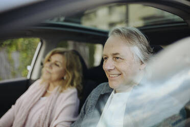 Smiling mature man sitting with woman in car seen through glass window - GMCF00162