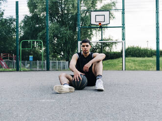 Basketballspieler mit Ball auf dem Spielfeld sitzend - ASGF00769