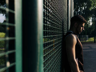 Athlete leaning on fence at basketball court - ASGF00773