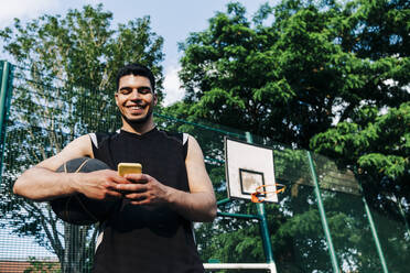 Lächelnder Sportler mit Smartphone auf dem Sportplatz - ASGF00774