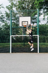Sportler, der einen Basketball in einen Reifen auf dem Platz eintaucht - ASGF00777