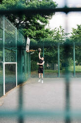 Junger Sportler spielt Basketball auf einem Sportplatz - ASGF00778