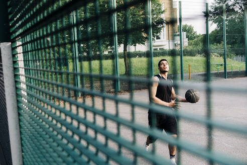 Basketballspieler beim Üben auf dem Sportplatz durch den Zaun gesehen - ASGF00779