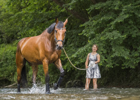 Junge Frau, die ein Pferd an der Longe führt und im Wasser plantscht - STSF02982