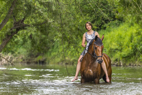 Junge Frau reitet auf einem Pferd in einem Fluss im Wald - STSF02986