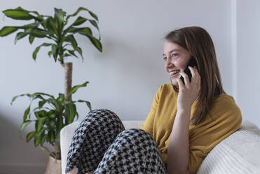 Young woman talking on smart phone while sitting on sofa at home - DSIF00462