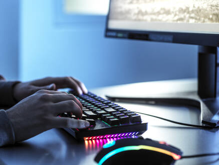 Teenage boy playing video game using keyboard on computer at table - ABRF00892