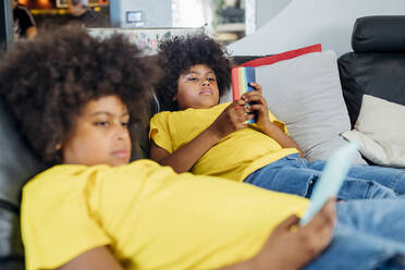 Twin brothers using wireless technologies on sofa at home - MEUF03399