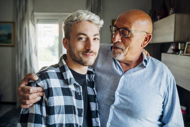 Father with arm around looking at son while standing at home - MEUF03404