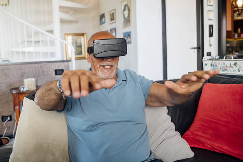Mann gestikuliert, während er eine Virtual-Reality-Brille zu Hause trägt - MEUF03421