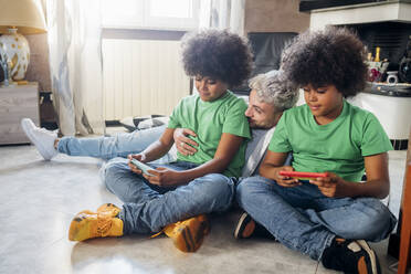 Junger Mann mit Zwillingsbrüdern benutzt sein Smartphone, während er zu Hause sitzt - MEUF03422