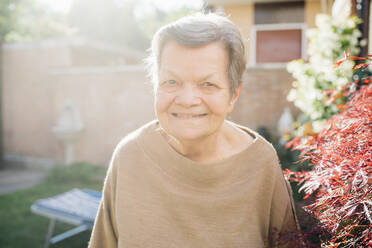 Ältere Frau lächelt in der Nähe der Pflanze im Hinterhof - MEUF03426