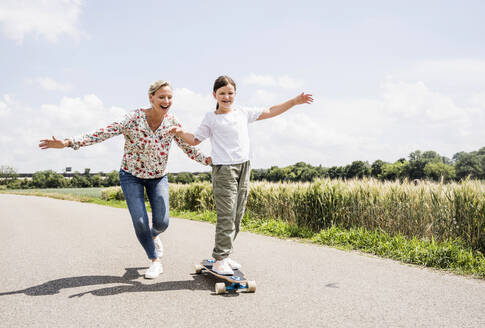 Mutter hilft Tochter auf dem Skateboard an einem sonnigen Tag - UUF23816