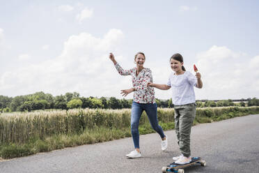 Lächelnde Frau läuft an einem Mädchen vorbei, das auf einem Skateboard steht - UUF23818