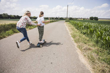 Mutter hilft ihrer Tochter beim Erlernen des Skateboardfahrens auf der Straße - UUF23819