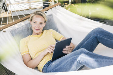 Thoughtful woman holding digital tablet while lying on back in hammock - UUF23833