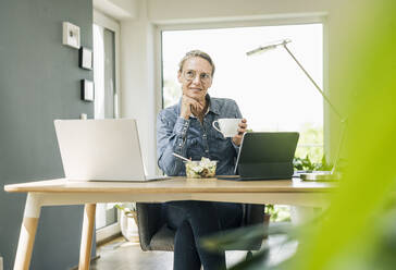 Businesswoman with hand on chin sitting at home office - UUF23839