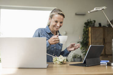 Lächelnde Geschäftsfrau, die Kaffee trinkt und auf ein digitales Tablet schaut - UUF23844