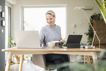 Female freelancer smiling while working at home office - UUF23859