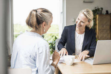 Geschäftsfrau erklärt Kunden, während sie im Büro sitzt - UUF23865