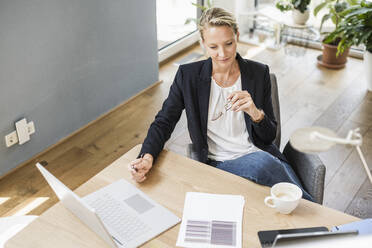 Geschäftsfrau mit Laptop und digitalem Tablet im Büro sitzend - UUF23870