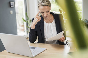 Geschäftsfrau mit Laptop bei der Überprüfung von Dokumenten während der Arbeit im Büro - UUF23874