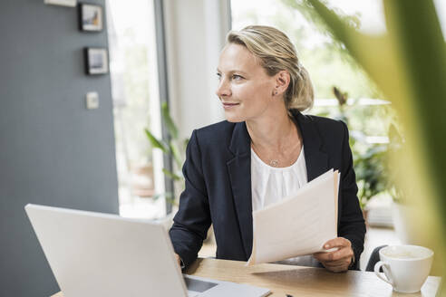 Thoughtful businesswoman with document and laptop at office - UUF23876
