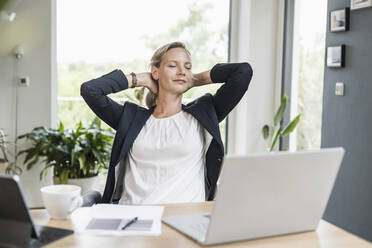 Businesswoman with hands behind head resting while sitting at office - UUF23877