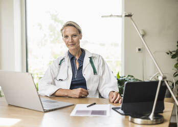 Confident female professional sitting by desk at office - UUF23892