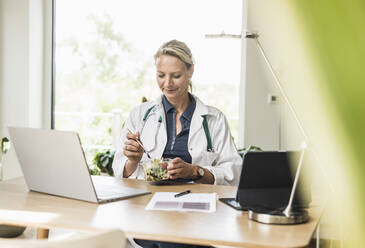 Doctor eating food while sitting at office - UUF23894