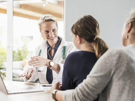 Lächelnder Arzt berät einen Patienten und eine Frau im Büro - UUF23901