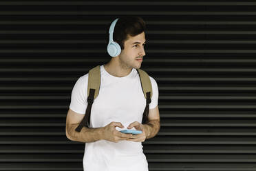 Young man with mobile phone looking away while standing in front of shutter - XLGF02069