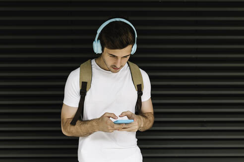 Mann mit Kopfhörern und Smartphone vor einem Fensterladen - XLGF02070