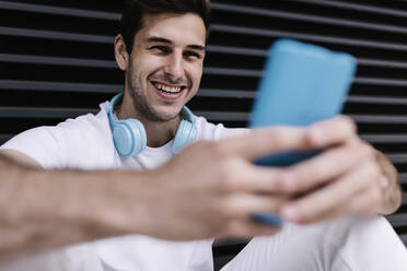 Happy man using smart phone while sitting in front of shutter - XLGF02075