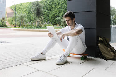 Junger Mann benutzt digitales Tablet auf Skateboard an Säule - XLGF02088