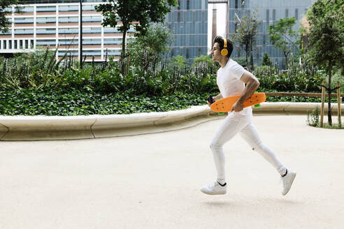 Junger Mann mit Skateboard läuft im Park - XLGF02095