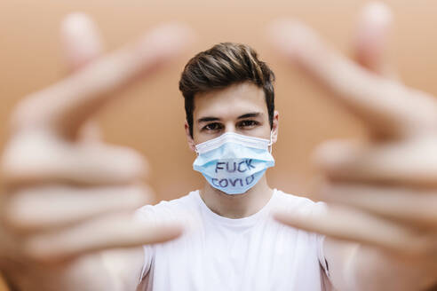 Man wearing protective face mask with text gesturing in front of wall - XLGF02102