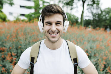 Lächelnder junger Mann hört Musik über Kopfhörer inmitten einer Wiese - XLGF02109