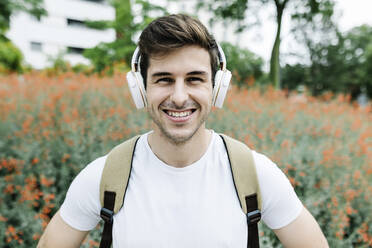 Smiling young man listening music through headphones amidst meadow - XLGF02109