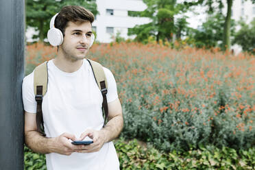 Mann mit Smartphone schaut weg, während er sich auf einen Mast stützt - XLGF02110