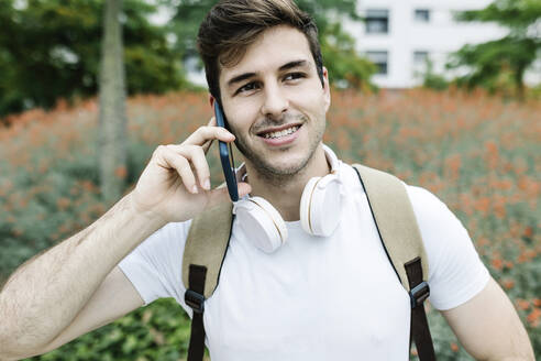 Lächelnder junger Mann, der wegschaut, während er mit seinem Smartphone telefoniert - XLGF02112
